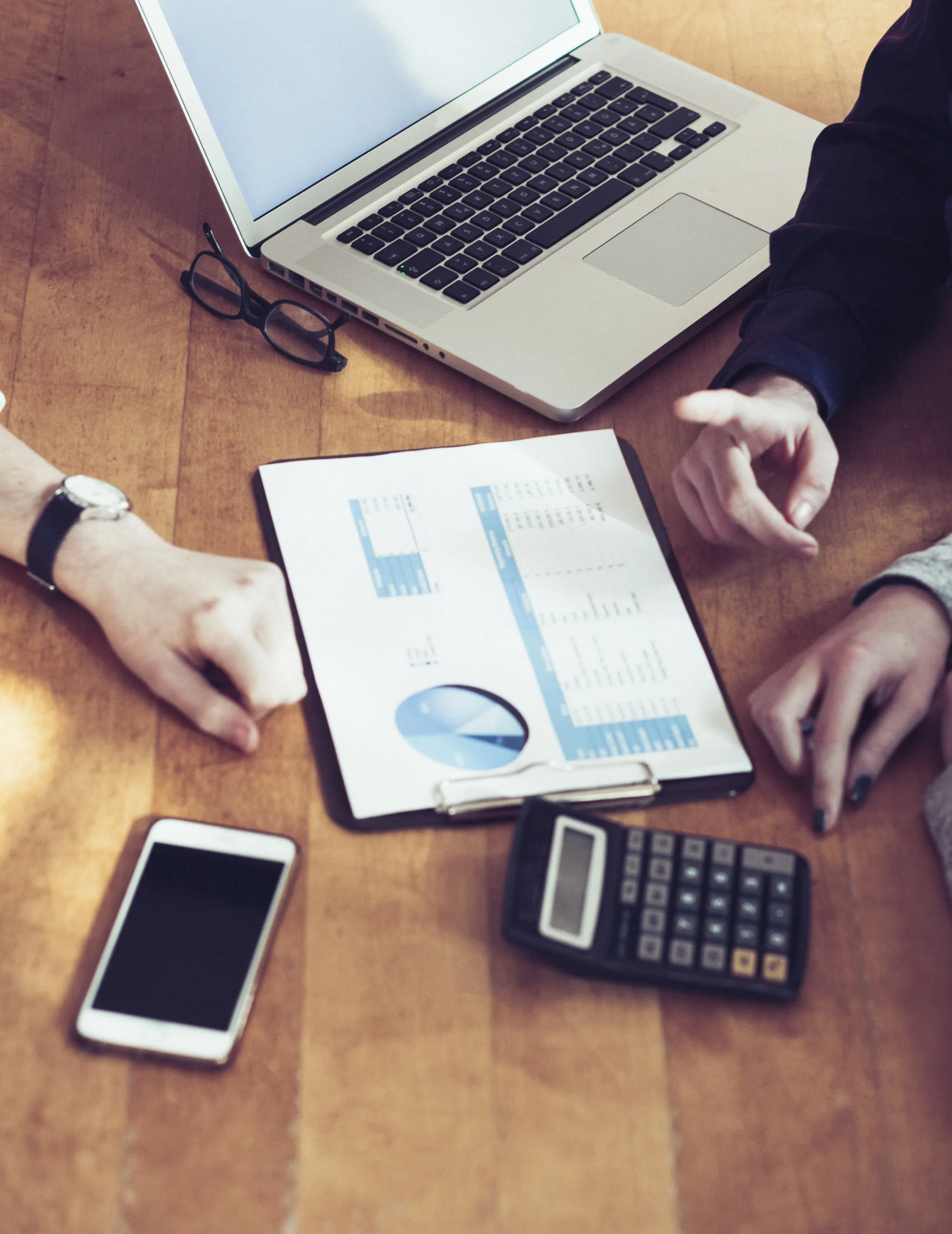 Business team reviewing financial reports with laptop, calculator, and smartphone on desk during strategic planning meeting.
