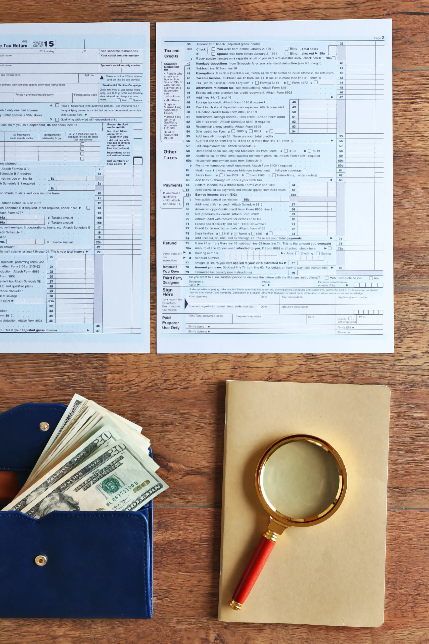 Individual tax return forms on wooden desk with cash in wallet and magnifying glass, representing tax review, filing, and financial analysis