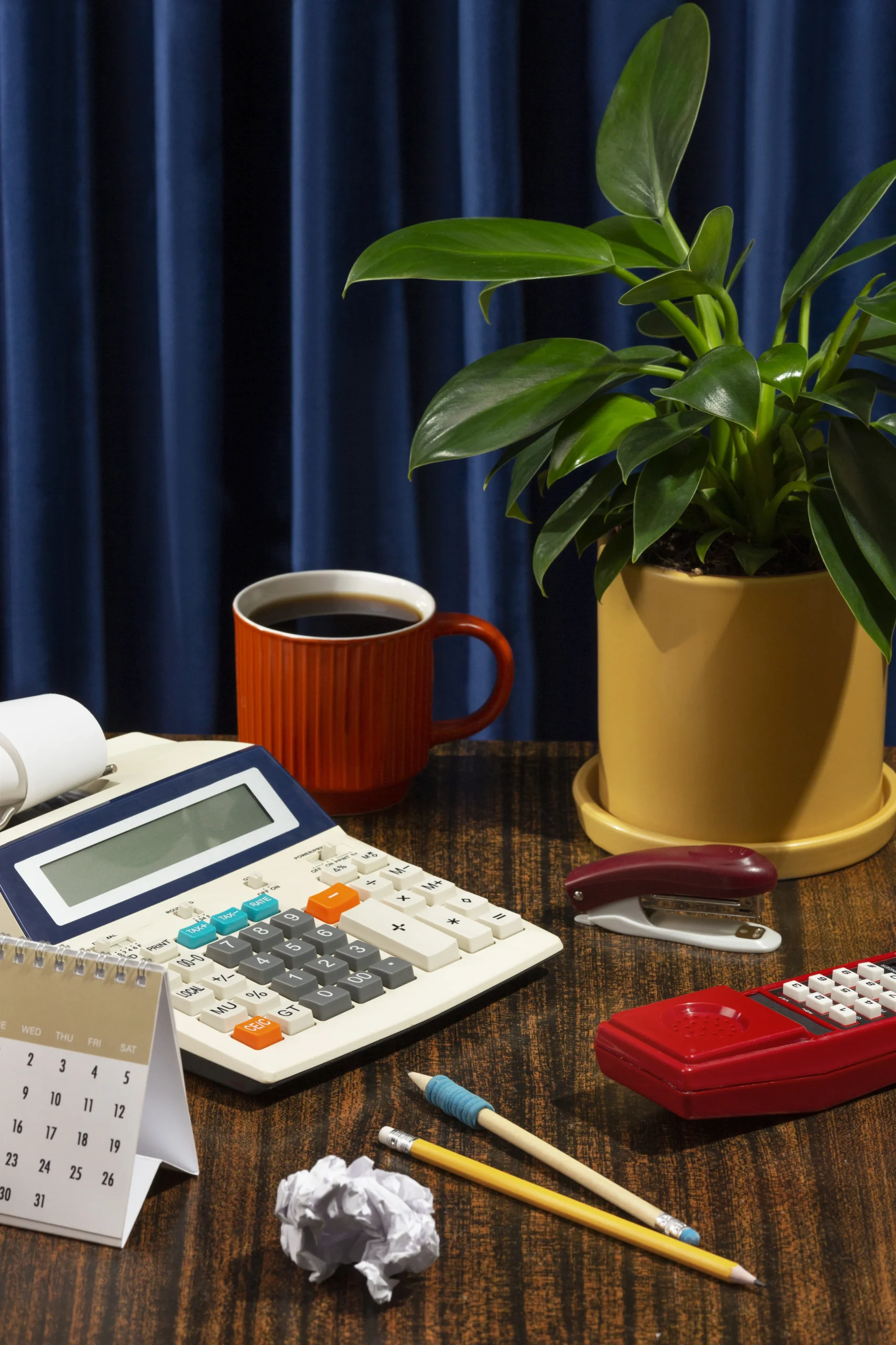 Office desk with calculator, coffee mug, potted plant, calendar, pencils, stapler, and notes, representing tax planning or accounting work